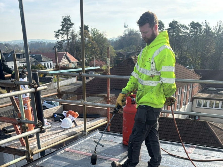 Founder of RunwiseOS on a real UK roofing site, wearing hi-vis and using a gas torch to install flat roofing membrane