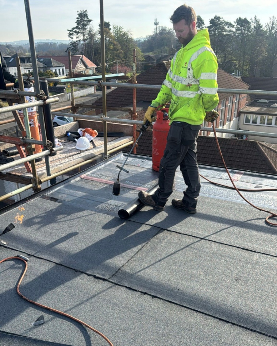 Founder of RunwiseOS on a real UK roofing site, wearing hi-vis and using a gas torch to install flat roofing membrane